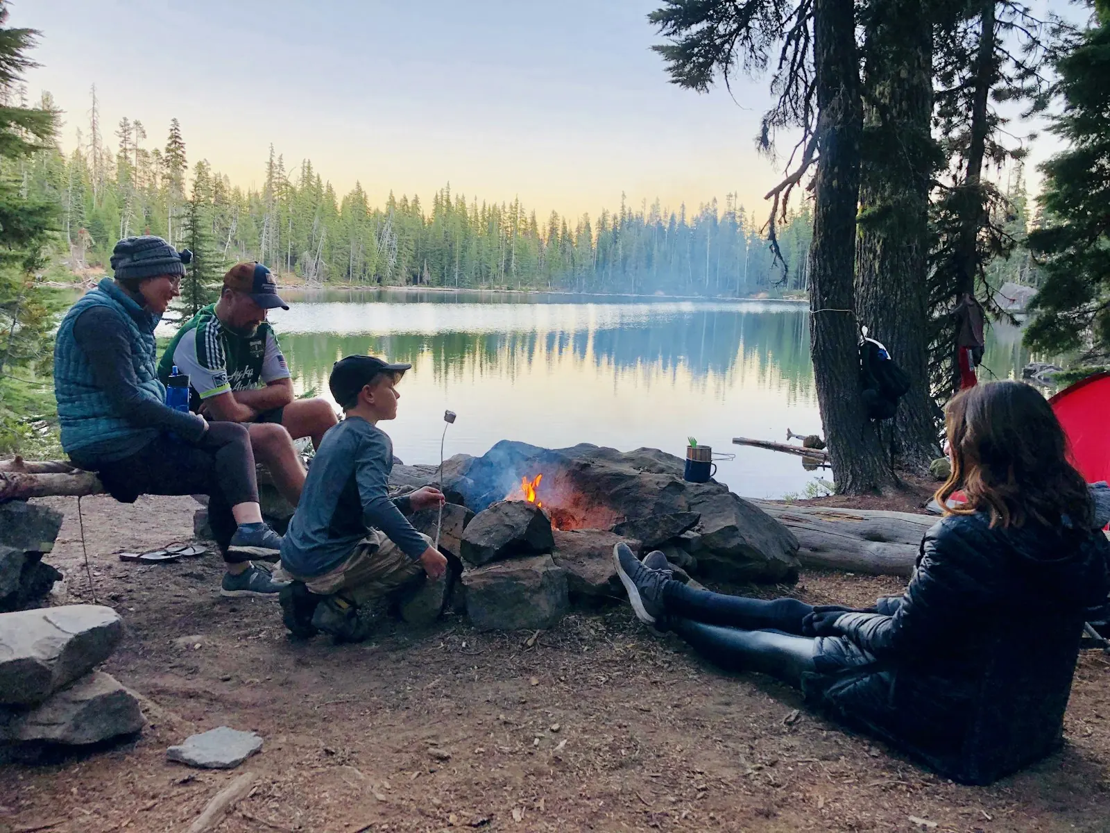 A family relaxing around a lakeside campfire at golden hour